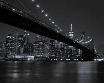 Illuminated bridge over river by buildings against sky at night