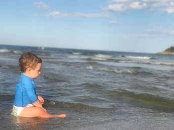 Side view of cute baby boy sitting on shore at beach