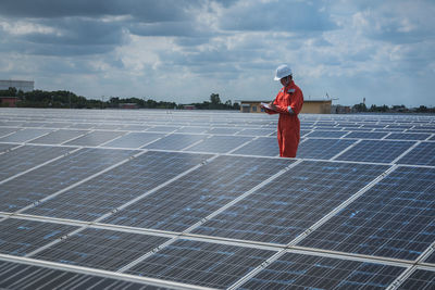 Engineer standing amidst solar panel against cloudy sky