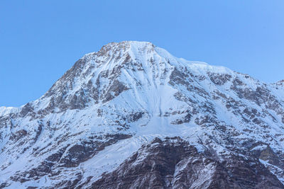 Low angle view of snowcapped mountains against clear blue sky