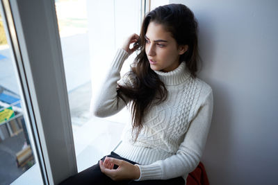 Young woman looking away while sitting by window