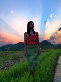 Young woman standing on field against sky during sunset