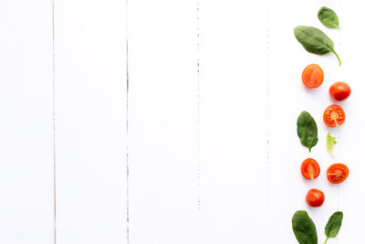 Flat lay with red cherry tomatoes and green spinach leaves on a white wooden background