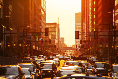 Cars on street amidst buildings in city during sunset