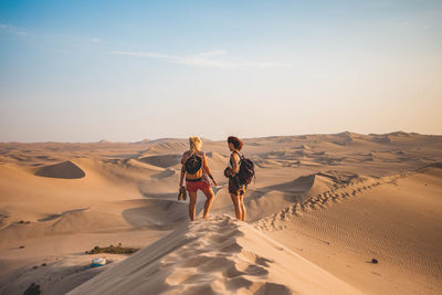 Rear view of friends walking on sand dune