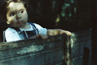 Girl looking away while standing against wooden fence