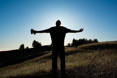 Silhouette man with arms outstretched standing on grassy field against sky