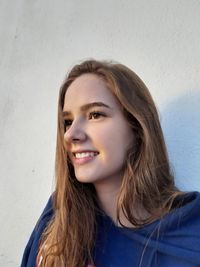 Smiling young woman looking away against wall