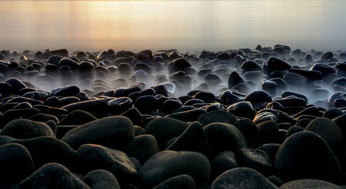 Close-up of rocks at sea shore against sky during sunset