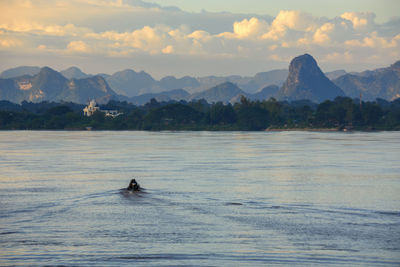 Man rowing boat in lake against sky