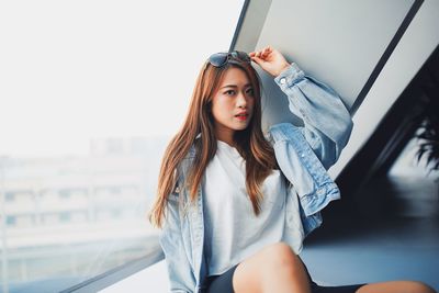 Portrait of young woman sitting against window