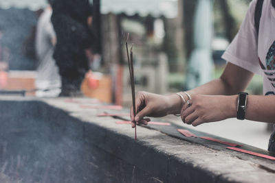Midsection of woman holding burning incense sticks at temple
