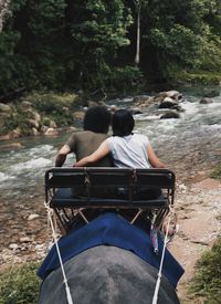 Rear view of couple sitting on elephant in forest during safari