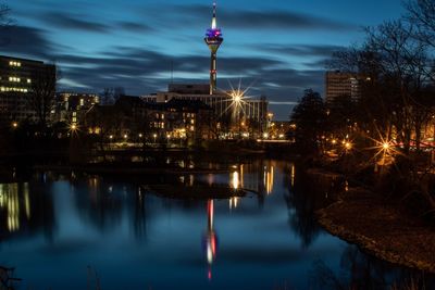 Illuminated buildings by river against sky at dusk