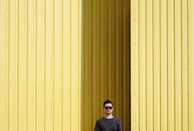 Portrait of man wearing sunglasses against yellow corrugated iron