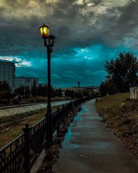 Street lights on road against cloudy sky