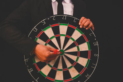 Midsection of businessman with dartboard standing against black background