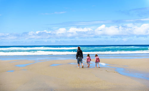 Rear view of woman with daughters walking at beach
