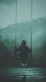 Rear view of man sitting on swing at playground