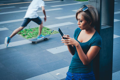 High angle view of young woman using mobile phone while standing by column in city