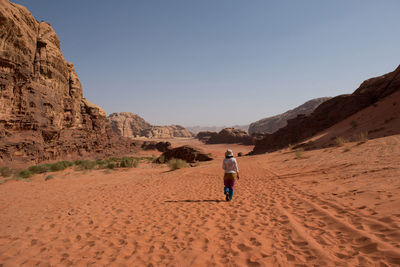 Full length rear view of woman walking on desert against clear sky