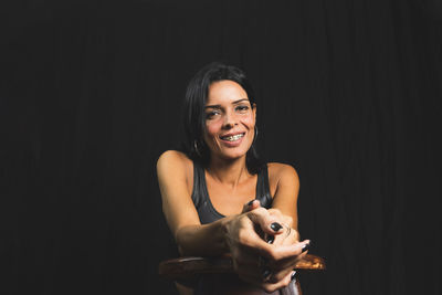 Portrait of young woman sitting against black background