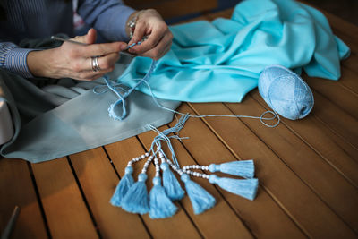 Craftswoman knits and assembles the braid, close-up. real light interior, wooden table, top view. 