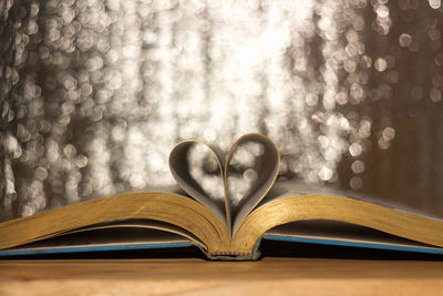 Close-up of heart shape pages on open book against illuminated lights