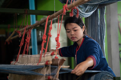 Young woman weaving textile on loom