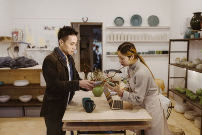 Male customer with smart phone talking to female potter while paying at workshop