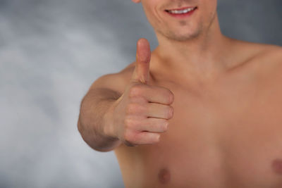 Midsection of shirtless man showing thumbs up sign against gray background