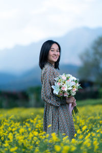 Young woman standing by yellow flower on field