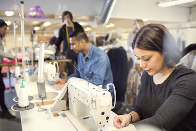 Concentrated woman sewing clothes while volunteers working at workshop