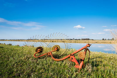 Agricultural machinery on grassy field by river against blue sky