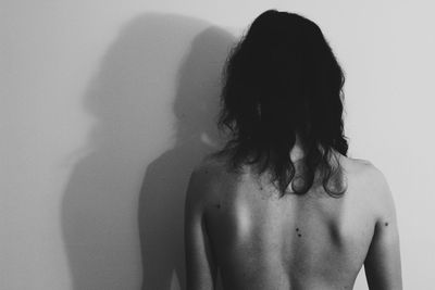 Rear view of shirtless woman standing against white background