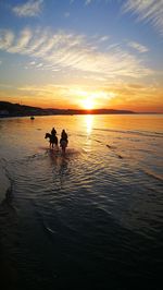 Silhouette people on sea against sky during sunset