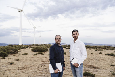 Confident engineers with tablet pc and laptop standing at wind farm