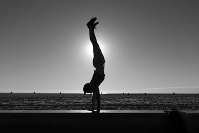 Full length of man performing handstand on beach against sky