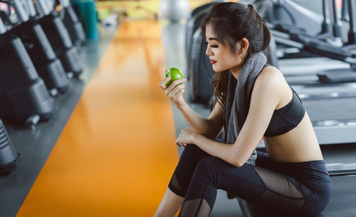 Woman holding granny smith apple while sitting on treadmill in gym