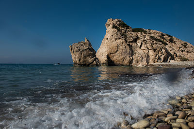 Rock formation in sea against clear blue sky