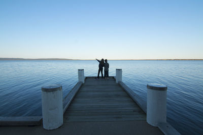 Rear view of two children on jetty against blue sky