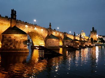 Arch bridge over river against buildings at night