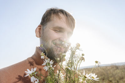 Smiling bearded man smelling chamomile flowers