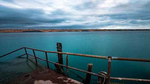 Railing on sea against cloudy sky