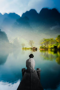 Rear view of man looking at lake against sky