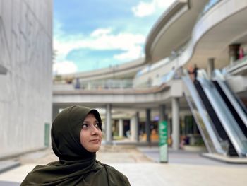 Portrait of young woman standing against built structure