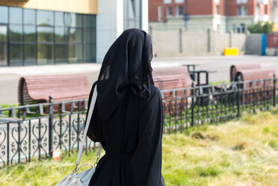 A muslim woman walking down a city street in a black national outfit, a view from the back.