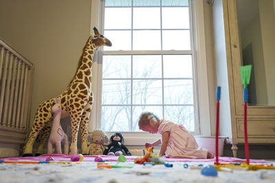 Toddler girl plays with toys alone in her room, in front of a window