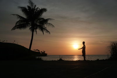 Silhouette man standing on beach against sky during sunset