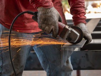 Midsection of man grinding metal at factory